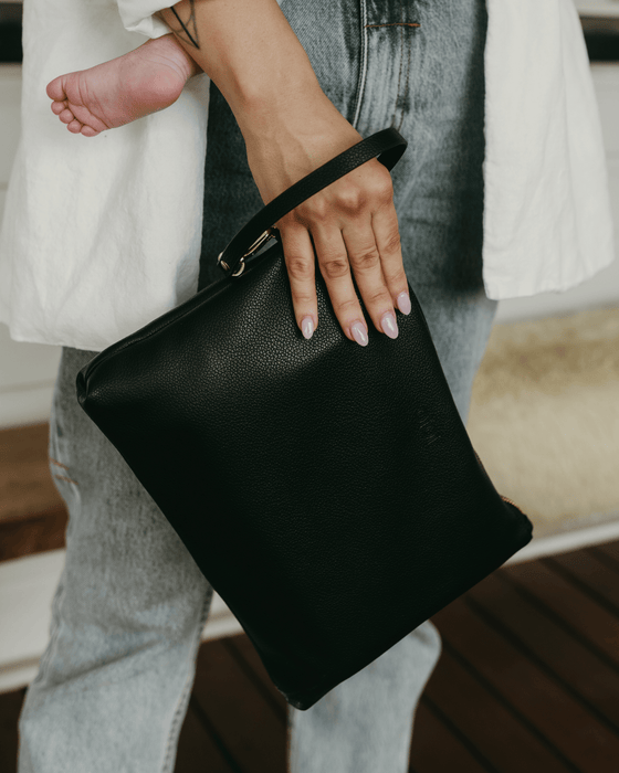 A woman holds onto a black vegan leather nappy wallet through the wristlet.