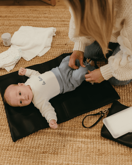 A baby boy is laying down on a black change mat waiting for his nappy to be changed.