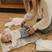 A mum getting ready to change her baby's nappy on the floor using a silver travel change mat.