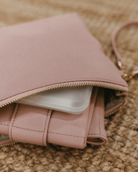 Spilling out of a pale pink nappy wallet are its contents: nappies, fold-up vegan change mat and a portable wipes case.