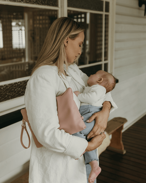 A mum cradles her baby boy to sleep, wearing a white blazer and pink bag.