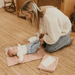 A baby is being changed on the floor, laying comfortably on a pretty pink change mat.